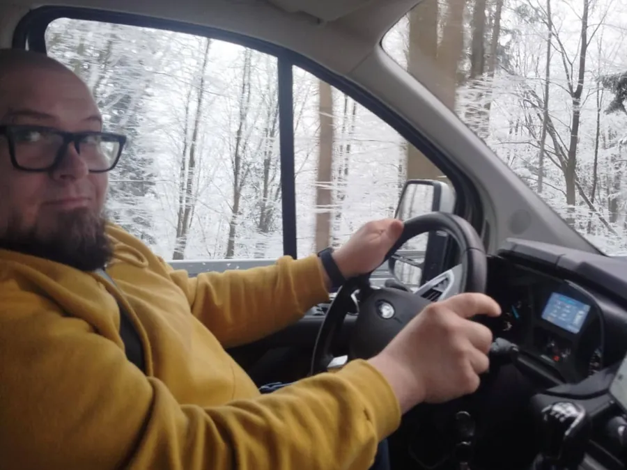 Maciej Gomułka za kierownicą samochodu w zaśnieżonym lesie, w drodze na pokaz